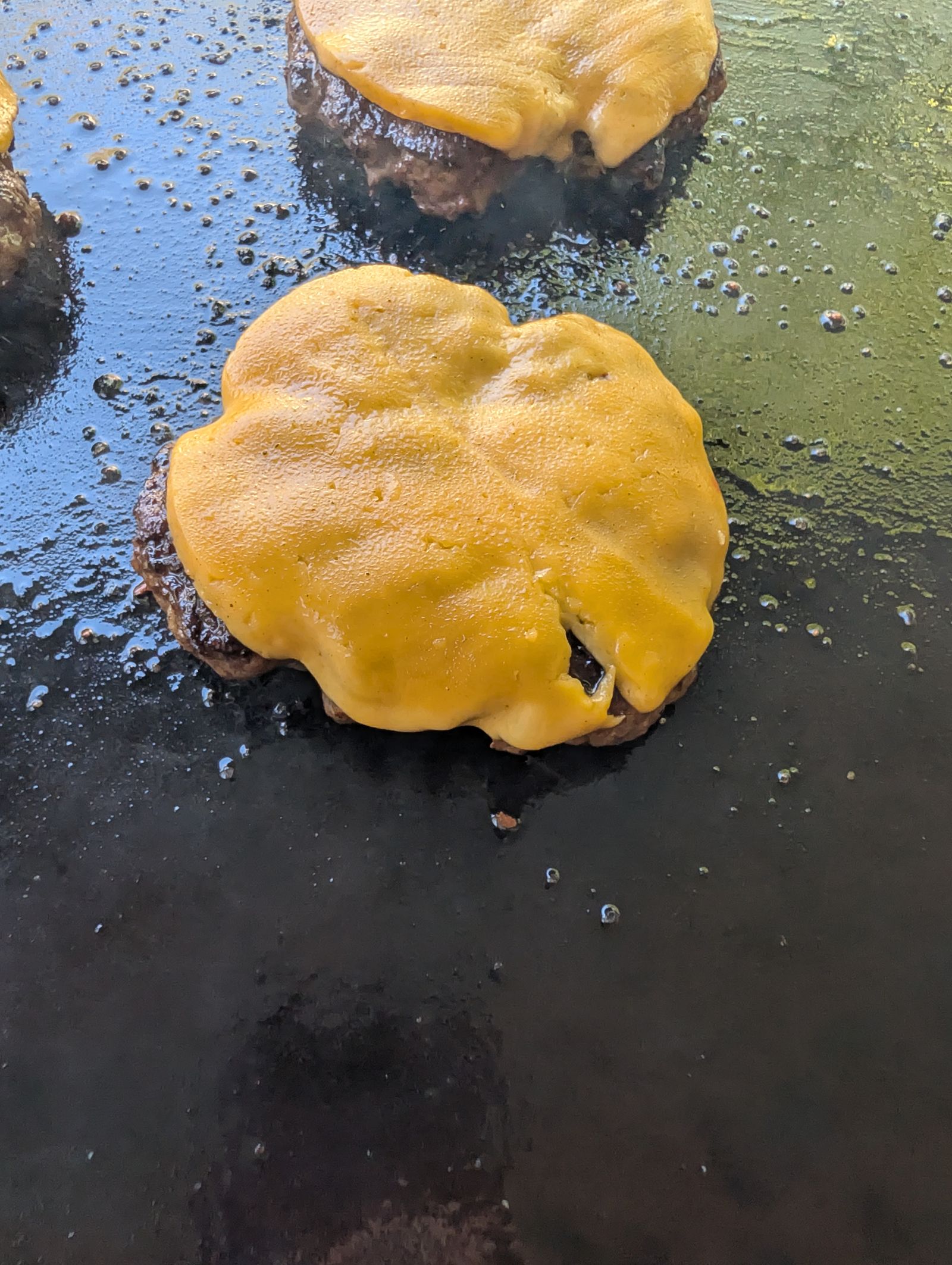Cheese melting over burgers on a Blackstone griddle