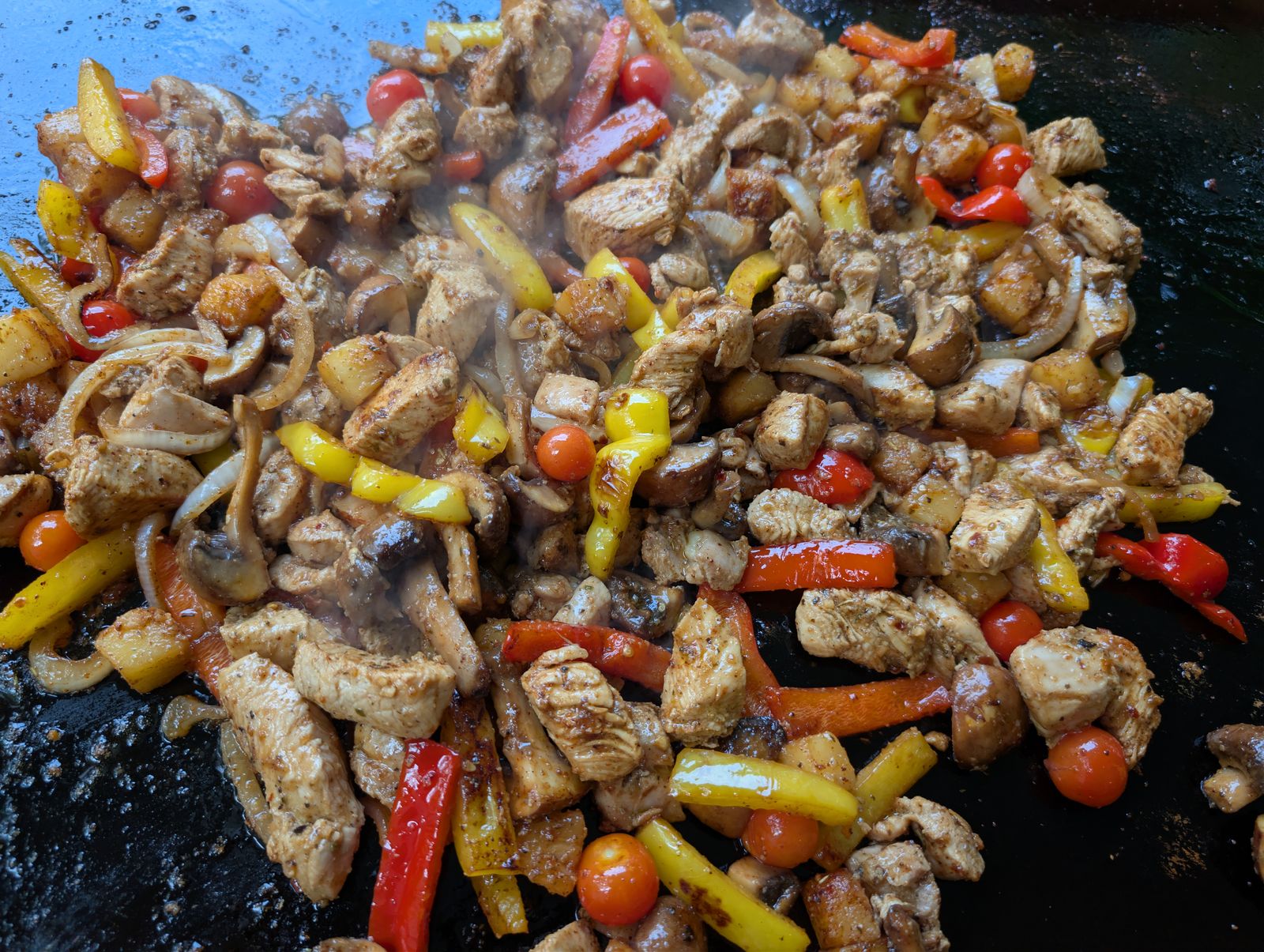 Chicken, peppers, pineapple, mushrooms, and cherry tomatoes all cooking together on the Blackstone, nearly finished