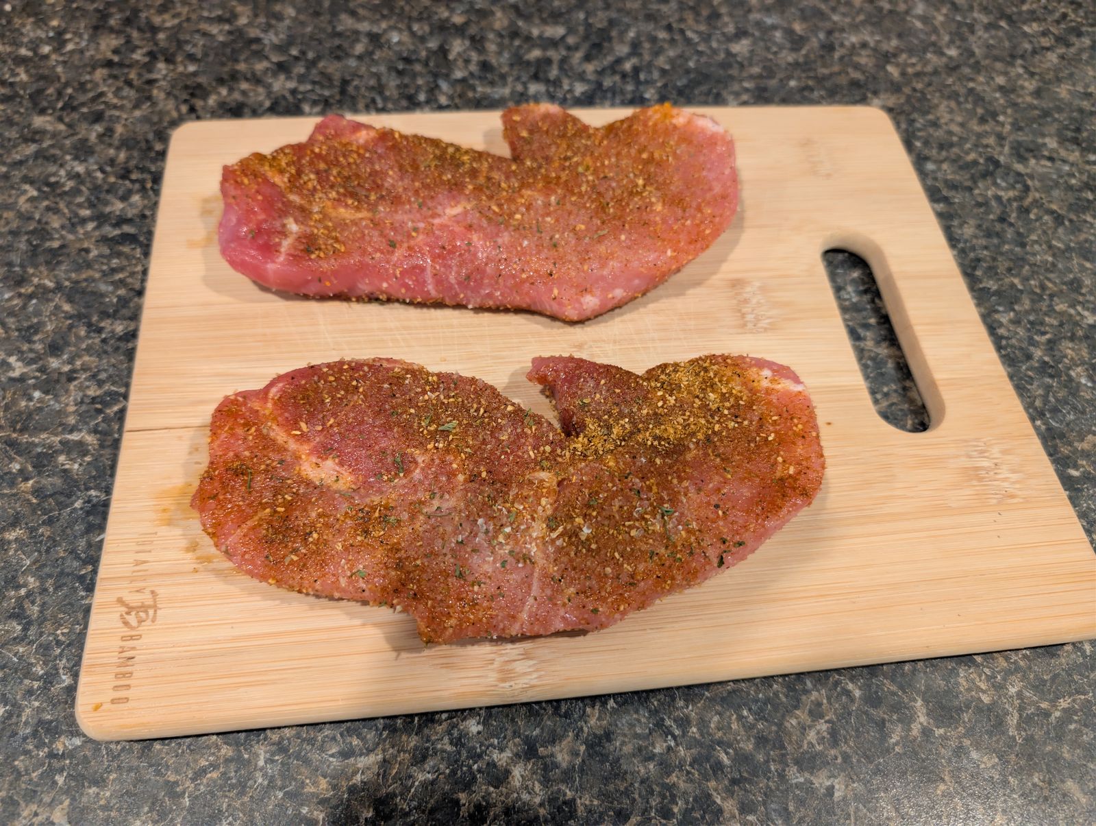 Raw pork steaks seasoned with Cajun seasoning and Lawry's Garlic Salt on a cutting board